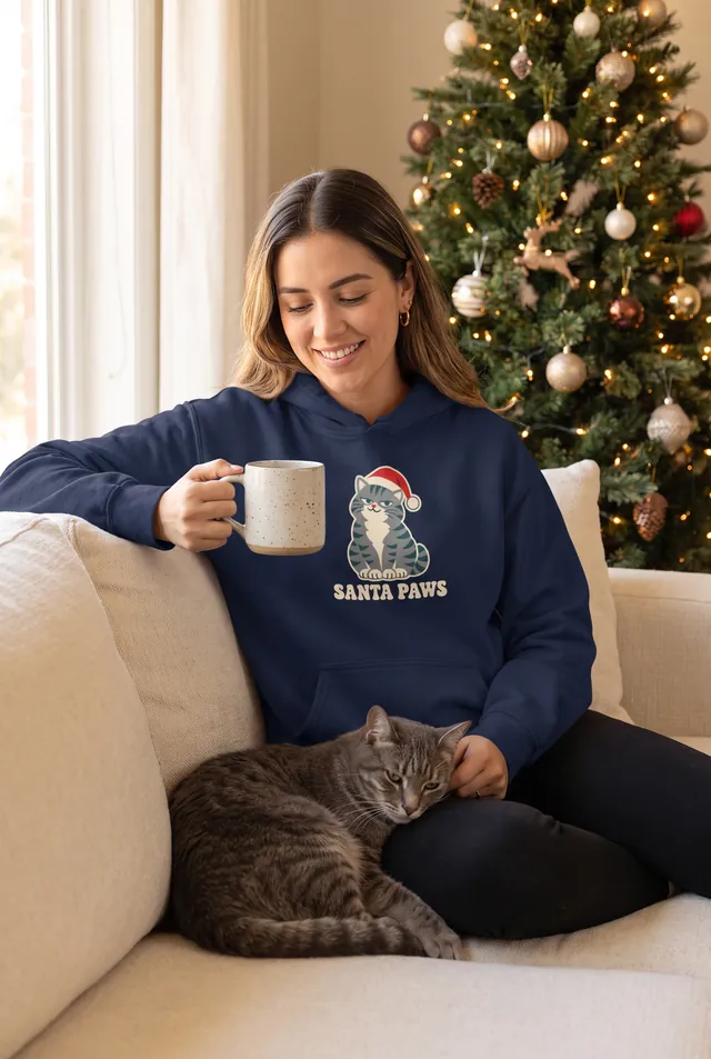 SANTA PAWS yazılı Noel şapkalı kedi baskılı lacivert hoodie giyen kadın, yanında kedisi